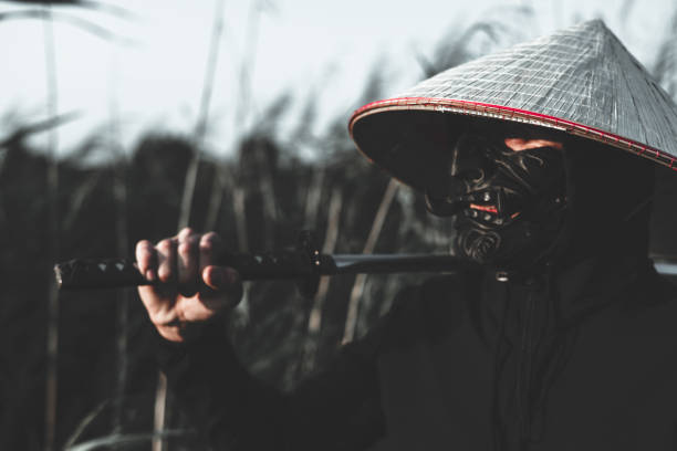 A masked samurai stands tall in a lush bamboo forest, clutching a gleaming katana, radiating strength and power with every move. Majestic samurai with katana in tall grass..