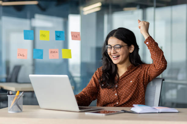 istock Happy office worker celebrating success at desk with laptop and sticky notes 2189564284