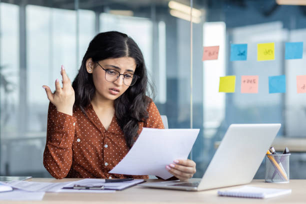 istock Stressed businesswoman reviewing documents at desk in modern office setting 2189568322
