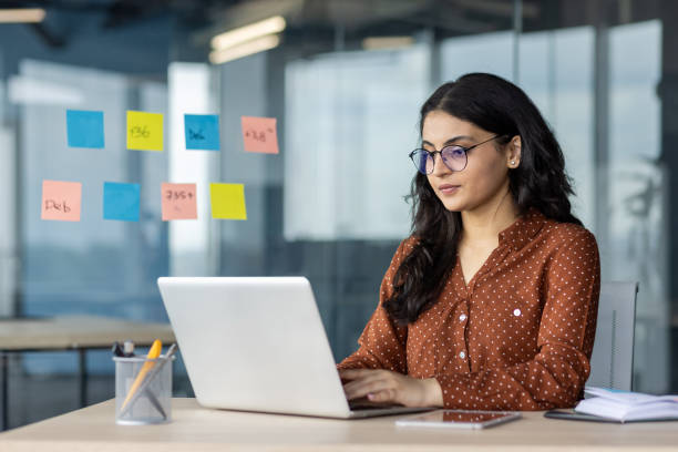 istock Focused office worker using laptop at desk with sticky notes on glass wall 2189568832