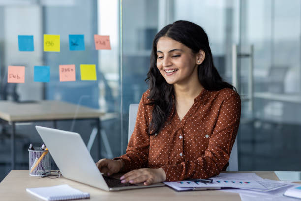 istock Smiling woman working on laptop in modern office environment with sticky notes 2189571871
