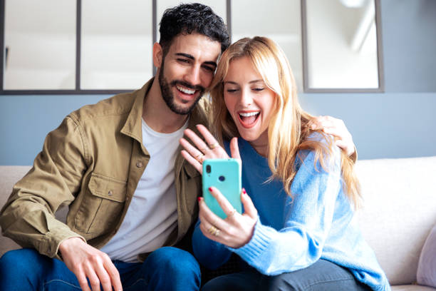 istock Excited couple video chatting on a smartphone while sitting on a cozy couch. 2189576987