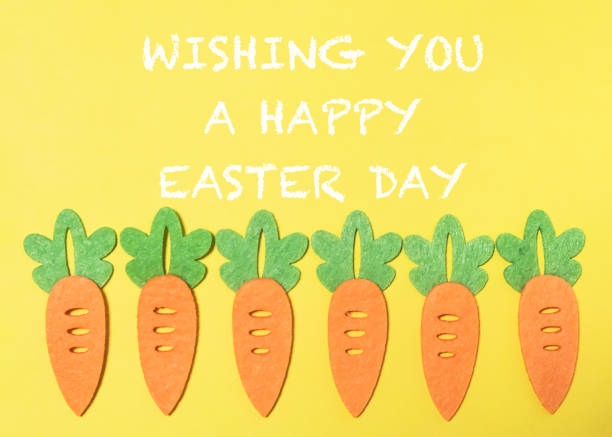 Group of carrots are arranged in a row on a yellow background. The carrots are decorated with green leaves, and the background is yellow. Concept of warmth and happiness
