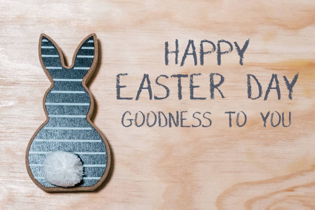Rabbit is on a wooden surface with the words Happy Easter Day written below it. The rabbit is decorated with a fluffy tail, and the background is a wooden surface. Concept of warmth and joy