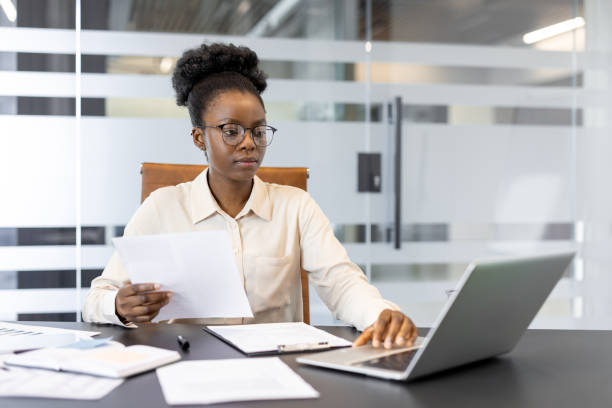 istock Focused businesswoman working with documents and laptop in modern office setting analyzing data and making notes 2189581618