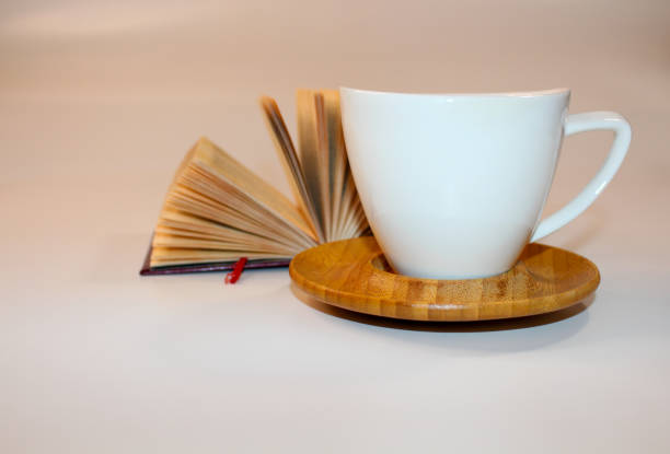 open book lies behind white cup on wooden stand on light background. High quality photo