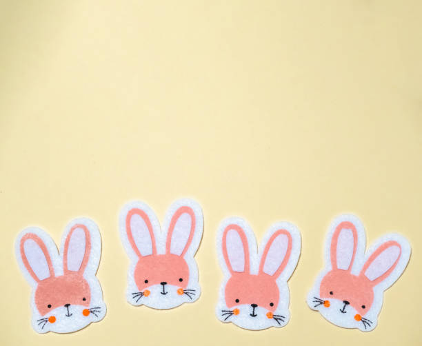 Four rabbits with pink faces are sitting on a yellow background. The rabbits are cute and playful, and the yellow background adds a warm and cheerful touch to the scene