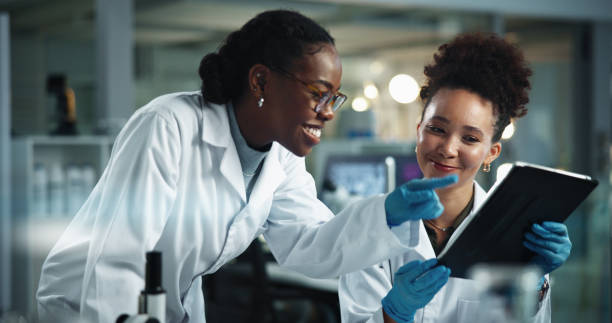 istock Science, women and tablet in lab for advice, positive feedback or pointing with problem solving at night. Team, tech and idea in facility for scientific study, pharmaceutical breakthrough or deadline 2189583492