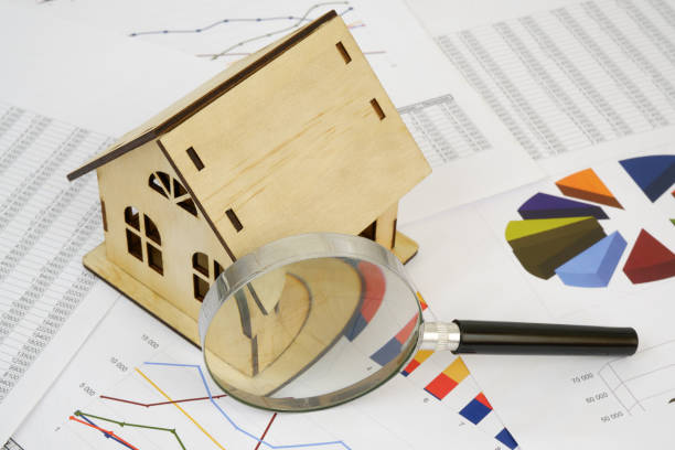 istock Wooden house with magnifying glass on financial data pages. 2189583665