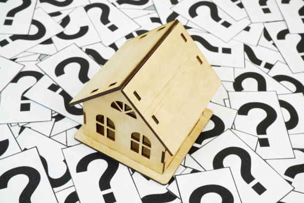 istock Wooden house model on question marks background. 2189583723