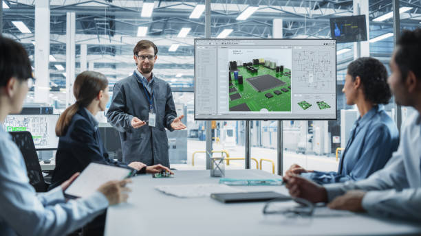 istock Electronics Factory Office Meeting: Caucasian Head Of Engineering Presenting Motherboard For New Powerful Microchips On TV Set. Diverse Managers And Technicians Listening and Planning Production. 2189584323