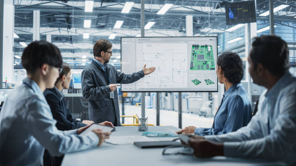 istock Electronics Factory Office Meeting: Caucasian Head Of Engineering Presenting Motherboard For Powerful Microchips On TV Set. Diverse Managers And Technicians Listening, Planning Production Process. 2189585480