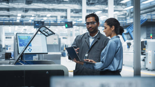 istock Indian Male Industrial Engineer And Hispanic Female Supervisor Using Laptop And Talking At Electronics Factory. Man Using Soldering Jet Printer, Explaining Process Behind Production Of Motherboards. 2189585635