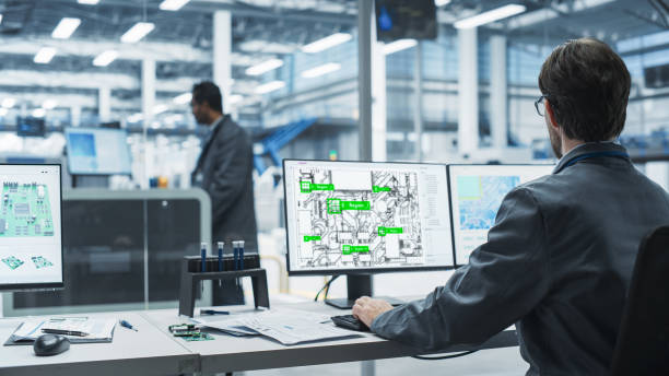istock Electronics Factory Office: Backview Of Asian And Caucasian Male Engineers Using Desktop Computers To Design Motherboards For Powerful Devices, While Indian Colleague Using Soldering Jet Printer. 2189585735