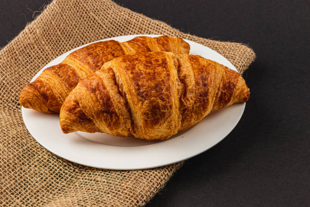 Two golden croissants on a white plate, perfect for a delightful breakfast