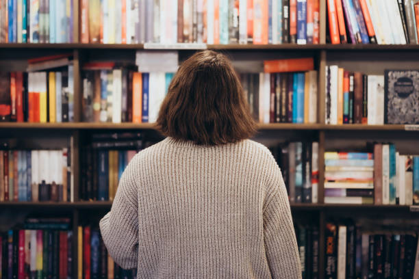 Young brunette woman choosing a book in a bookstore, back view.
