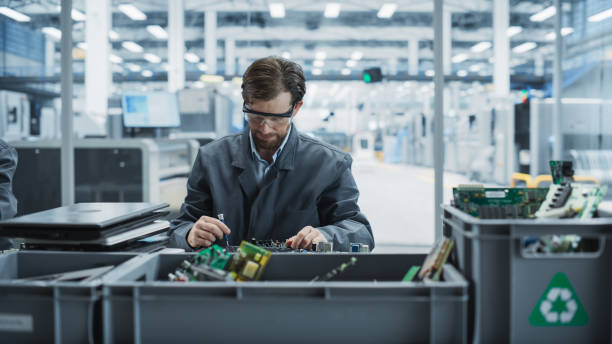 istock Caucasian Male Worker Disassembling Old Laptops To Recycle Electronic Components For Sustainable Microchip Production At an Electronics Factory. Man Unscrewing Motherboards And Sorting Parts In Boxes. 2189587650