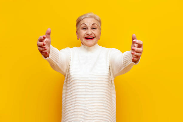 istock old grandmother in a white sweater pulls her hands forward to hug on a yellow isolated background 2189591454