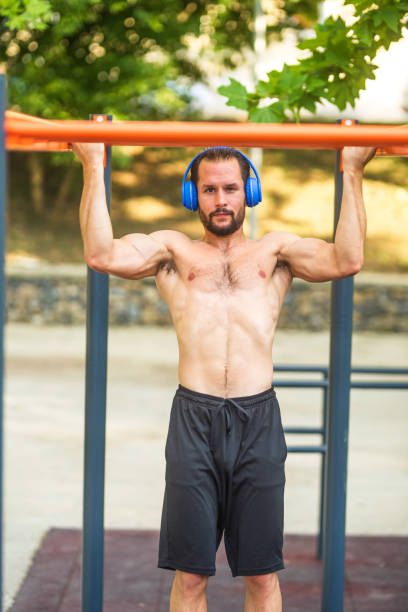 istock Young man wearing headphones doing pull ups in an outdoor gym 2189594952