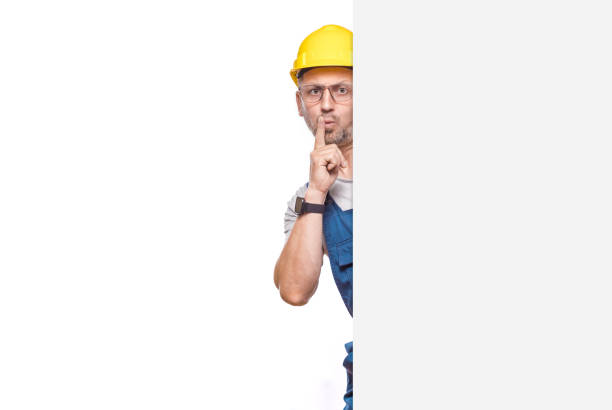 istock Hush. Construction worker holding finger on lips, keep the secret concept, isolated on white background. Craftsman against white wall 2189595742