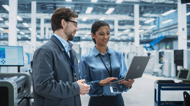 istock Caucasian Man and Hispanic Female Having a Conversation at an Industrial Facility. Advanced Factory Employees Working Together, Using Laptop for Supervising Assembly Process Of New Devices. 2189596917