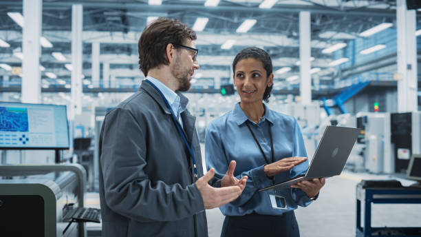 istock Caucasian Man and Hispanic Female Having a Conversation at an Industrial Facility. Advanced Factory Employees Working Together, Using Laptop Computer for Supervising Assembly Process Of New Devices. 2189596943