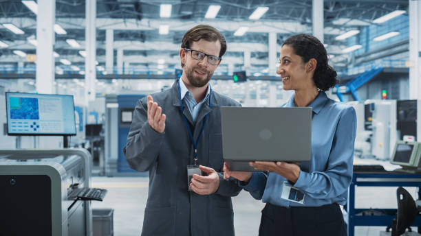istock Caucasian Man and Hispanic Female Having a Conversation at Industrial Facility. Advanced Factory Employees Working Together, Using Laptop Computer for Supervising Work Process At an Assembly Line. 2189596983