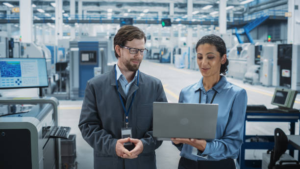 istock Caucasian Man and Hispanic Female Having a Conversation at an Industrial Facility. Advanced Factory Employees Working Together, Using Laptop Computer for Supervising Work Process At Assembly Line. 2189597043