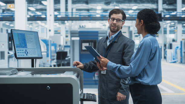 istock Male Technician and Hispanic Businesswoman Using Tablet Computer In Electronics Factory. Caucasian Man Explaining Production Of Motherboards For AI Powered Devices With Soldering Jet Printer. 2189597702