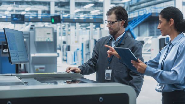 istock Male Technician and Hispanic Businesswoman Using Tablet Computer In Electronics Factory. Caucasian Man Explaining Production Of Motherboards For AI-Powered Devices With Soldering Jet Printer. 2189597721
