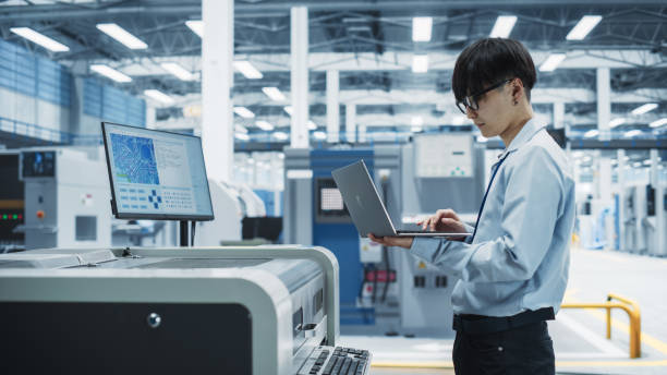 istock Asian Male Engineer Using Laptop To Control Soldering Jet Printer On Modern Electronics Factory. Man Working On Production Of Innovative Printed Circuit Boards For Artificial Intelligence Systems. 2189598210