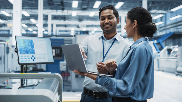 istock Indian Male Engineer And Hispanic Female Supervisor Using Laptop And Talking At Electronics Factory. Man Using Soldering Jet Printer, Explaining Process Behind Production Of Circuit Boards. 2189598444