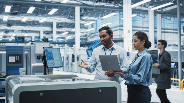 istock Indian Male Industrial Engineer And Hispanic Female Manager Using Laptop And Talking At Electronics Factory. Man Using Soldering Jet Printer, Explaining Process Behind Production Of New Circuit Boards 2189598523