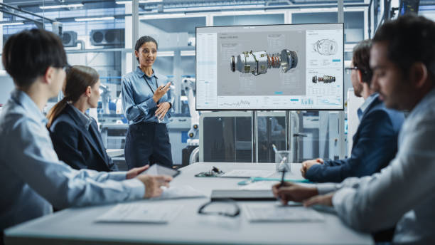 istock Electronics Factory Office Meeting: Hispanic Female Project Manager Presenting Innovative Engine On TV. Engineers And Technicians Listening, Taking Notes, and Generating Ideas For the Production. 2189598971