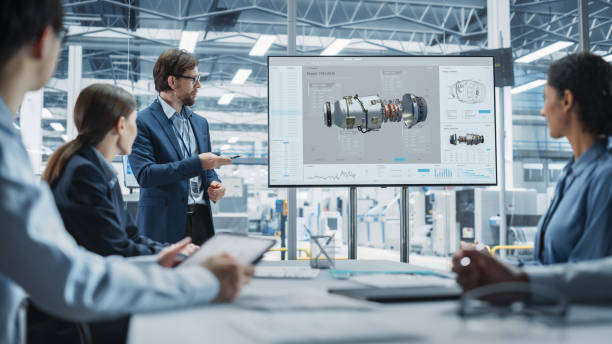istock Electronics Factory Office Meeting: Caucasian Male Project Manager Presenting Innovative Engine On TV. Diverse Engineers And Technicians Listening, Taking Notes, Generating Ideas For the Production 2189599151