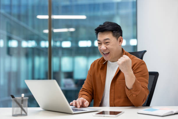 istock Asian man businessman celebrating success on laptop while working in modern office environment, reflecting achievement, motivation, and business success, expressing positive emotions 2189600274