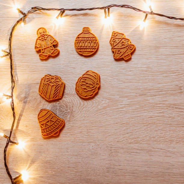 A charming display of gingerbread cookies aligned in a row surrounded by festive string lights on a wooden surface, evoking the warm and cozy holiday atmosphere of Christmas celebrations.
