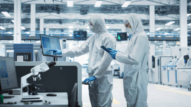 istock Two Scientists in Sterile Suits Walking In Electronics Factory Research Center. Technician With Tablet And Engineer Approaching Soldering Jet Printer And Starting Production Process Of Motherboards 2189603559