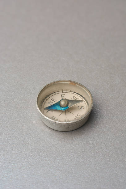 small round vintage pocket compass isolated on gray textured background, white dial with markings for cardinal directions and points towards north