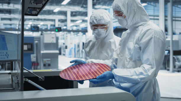 istock Semiconductor Production Process At Electronics Factory: Two Scientists In Sterile Suits Taking Out Silicon Wafer From Soldering Jet Printer And Checking It. Engineers Creating Hardware For Computers. 2189604384