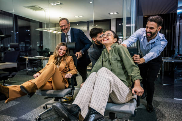 istock Playful scene in a modern office with businesspeople engaging in a friendly competition. In the image, colleagues are playfully pushing each other on office chairs 2189607923
