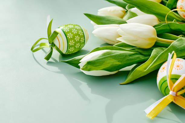 White tulips and easter eggs on green pastel background. Floral image with space for text for  Easter and other spring celebration.