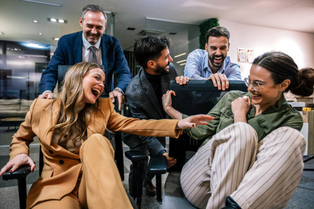istock Playful scene in a modern office with businesspeople engaging in a friendly competition. In the image, colleagues are playfully pushing each other on office chairs 2189608363