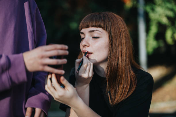 istock Young woman applying lipstick outdoors with assistance from a friend 2189608836