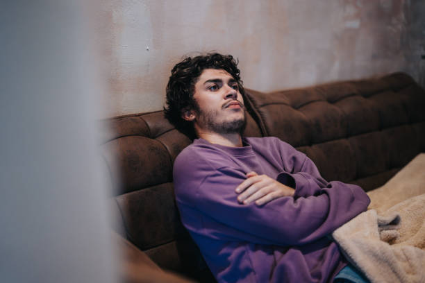 Young man relaxing on sofa wearing a purple sweatshirt, thoughtful mood captured