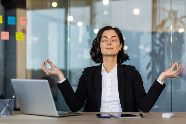 istock Professional woman meditating at desk in modern office environment, practicing mindfulness and relaxation during workday, promoting mental health and wellness with technology nearby for productivity 2189609565