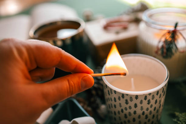 istock A hand lighting a festive candle with a matchstick, surrounded by pinecones, marshmallows, and evergreen branches, creating a warm and cozy Christmas atmosphere 2189609672