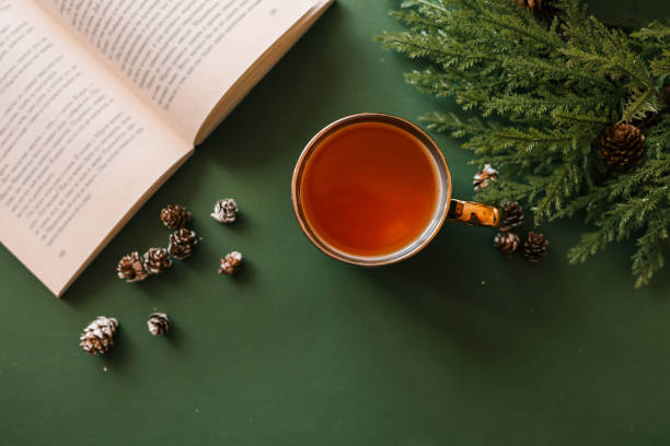 istock A cup of tea on a green surface with an open book, pinecones, and evergreen branches, creating a cozy and festive holiday atmosphere. Warm light and seasonal decor enhance the mood 2189609683