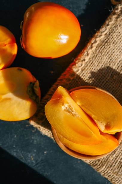 istock Sliced and whole persimmons arranged on a dark textured surface with natural light and burlap, showcasing vibrant colors and rustic simplicity. Perfect for food, seasonal, and healthy living themes 2189609972