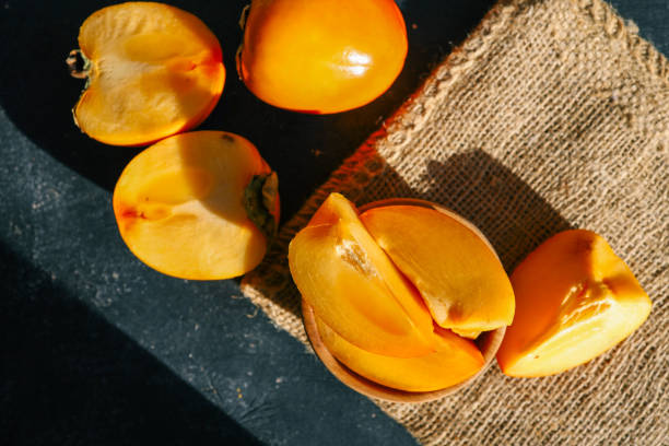 istock Sliced and whole persimmons arranged on a dark textured surface with natural light and burlap, showcasing vibrant colors and rustic simplicity. Perfect for food, seasonal, and healthy living themes 2189609979